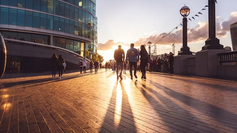 People walking across a sunlit plaza between modern glass office buildings at sunset